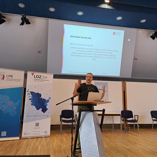 Wissenschaftlicher Referent Leon Brandt gibt dem Netzwerk des Landesdemokratiezentrums Impulse und hält einen Vortrag am Rednerpult