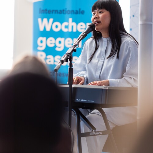 Die Sängerin Another Nguyen sitzt am Klavier auf der Bühne zu der Eröffnung der Internationalen Wochen gegen Rassismus